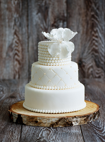 Wedding cake covered with white fondant, decorated with beads and hand-made flower on top