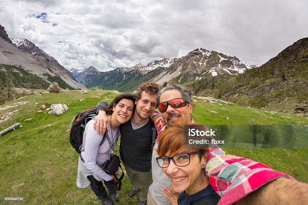 Selfie in scenic high altitude landscape on the Alps Four young people taking selfie on the Alps with snowcapped mountain range and dramatic sky in background. Scenic fisheye distortion. Concept of traveling people and nature beauty exploration. Fish-Eye Lens Stock Photo