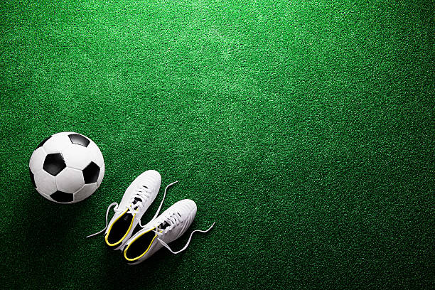 Soccer ball and cleats against green artificial turf, studio sho Soccer ball and cleats against artificial turf, studio shot on green background. Flat lay, copy space. studded footwear stock pictures, royalty-free photos & images