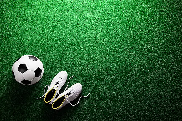 Soccer ball and cleats against artificial turf, studio shot on green background. Flat lay, copy space.