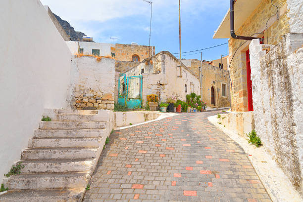Istanbul, Turkey – October 17, 2025: Steep neighborhood lane on Kınalıada with white single-storey houses, blue metal railings, stone retaining walls, overhead utility wires, and a parked motorcycle under bright daylight.