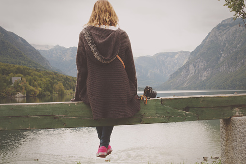 Girl sitting on a wooden pier near water.