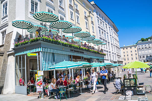  Salzburg, Austria - May 26, 2016: A local portrait artist displays his work on the sidewalk in front of an al fresco restaurant where diners enjoy lunch on uppper and lower levels overlooking the Old Market  (Alter Markt) square in Salzburg