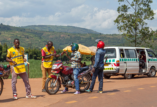 Gicumbi, Rwanda - June 3, 2016: taxi stop along the RN3 Byumba - Kigali road with motor taxi's, a minivan and several drivers; in the background cultivated hills