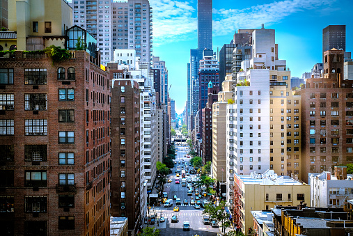 A colorful street canyon in New York City. The blue sky along with some clouds build a nice background for the busy street.