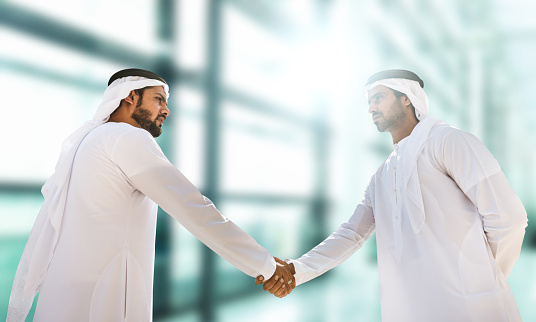 Arab Businessman shaking hands together. Teamwork business partner wear Muslim dress Shake Hands with Partnership Concept. Success UAE diversity people trust make commitment by handshake