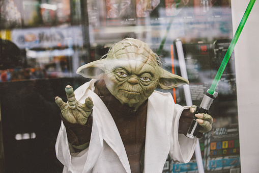 Paris, France - April 28, 2016: Portrait of Jedi Master Yoda toy model with green lightsaber on window display in Paris. Yoda is a fictional character in the Legend Star Wars Film franchise created by director George Lucas