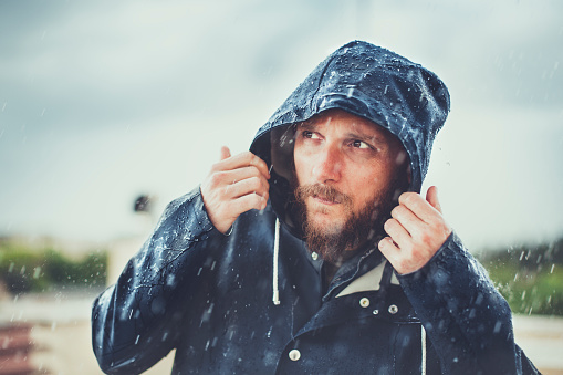 Hombre con gabardina todoterreno bajo una intensa lluvia photo