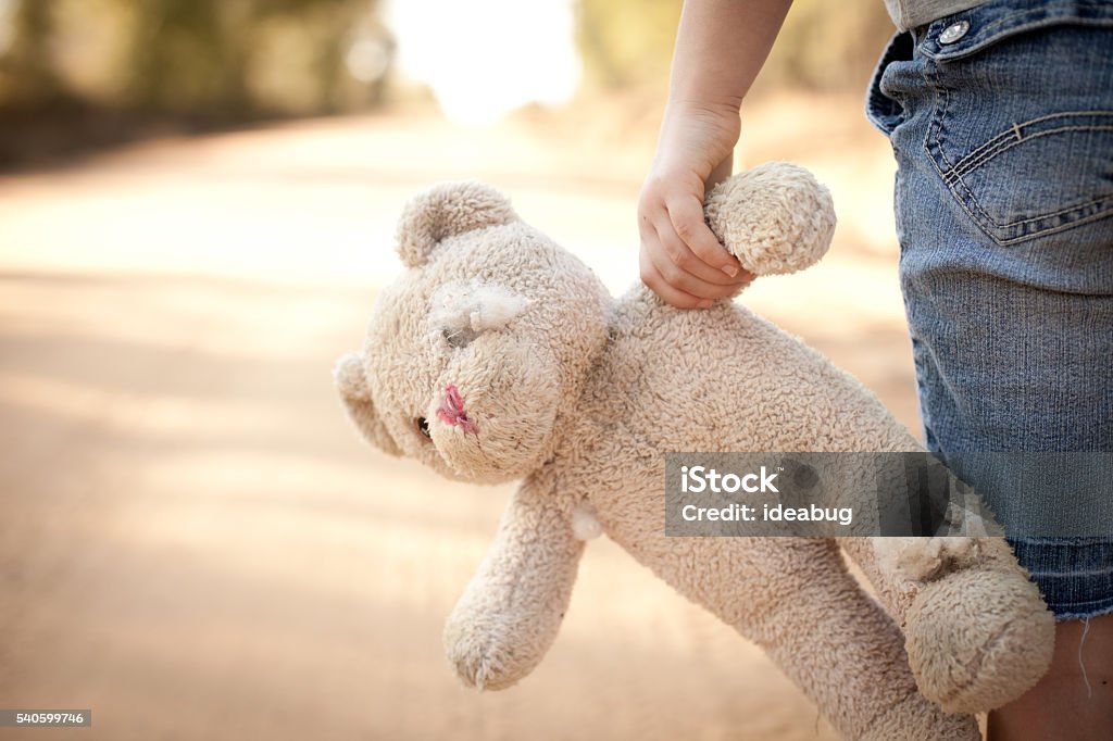 Runaway or Lost Girl Holding Old, Ragged Teddy Bear Color stock photo of a little runaway girl holding an old teddy bear at the side of a dirt road in the rural country. Child Stock Photo