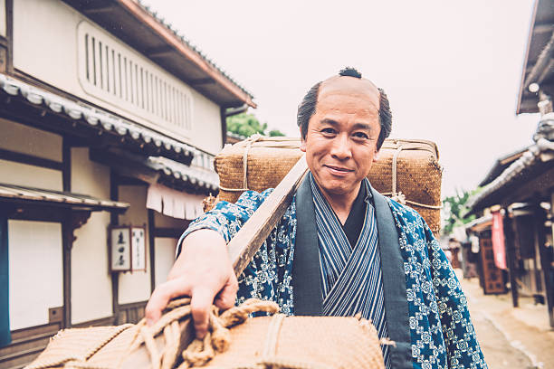 Portrait of a smiling japanese man, peasant, manual worker, carrying heavy burden on a stick on his shoulder. He is walking on the street of an old japanese town. Outdoors, copy space. Nikon D800, full frame, XXXL. iStockaLypse Kyoto 2016.
