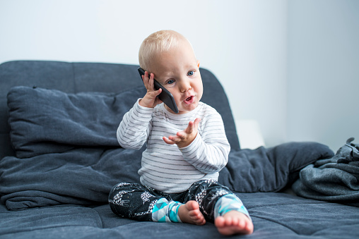 Cute young little boy talking on mobile phone. He is sitting a sofa and is focused.