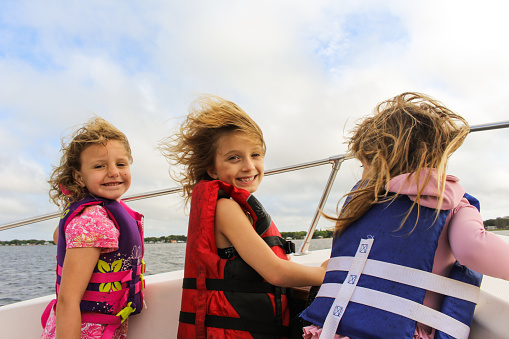 Three little girls wear life jackets on a boat