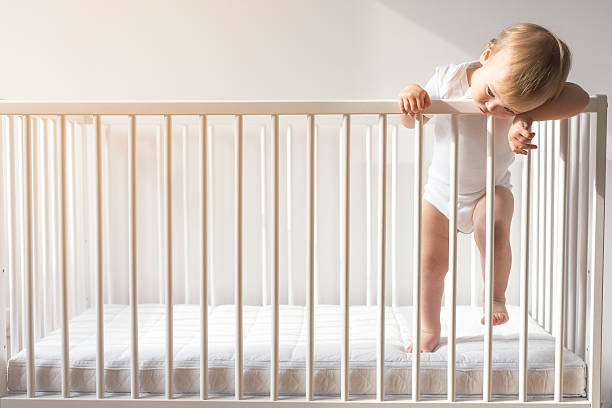 portrait of a bored baby standing in a crib. - babybox stockfoto's en -beelden