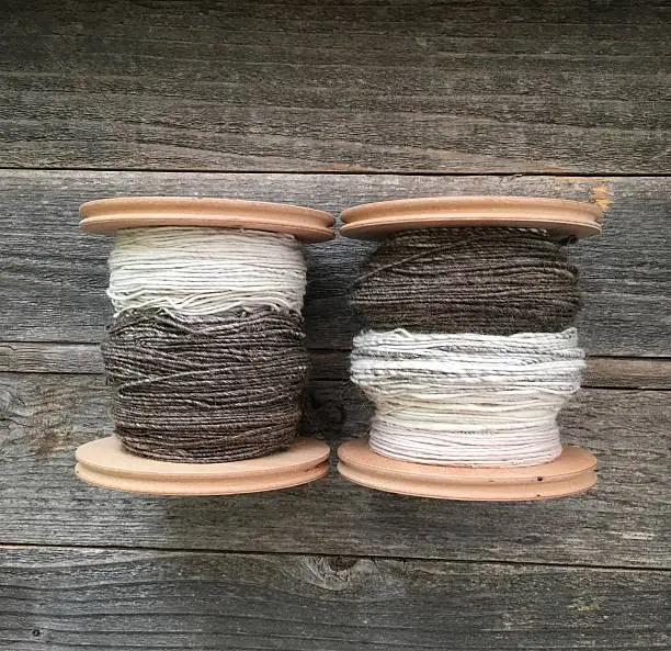 Two bobbins of handspun wool yarn on a wood surface.