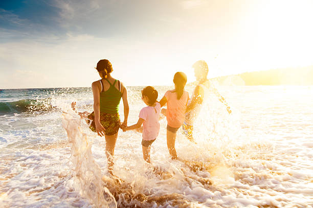 glückliche junge familie spielen am strand während dem sonnenuntergang - strandurlaub stock-fotos und bilder