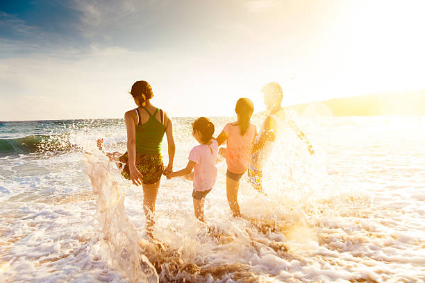 familia joven feliz jugando en la playa al anochecer - spraying beaches summer sunlight fotografías e imágenes de stock