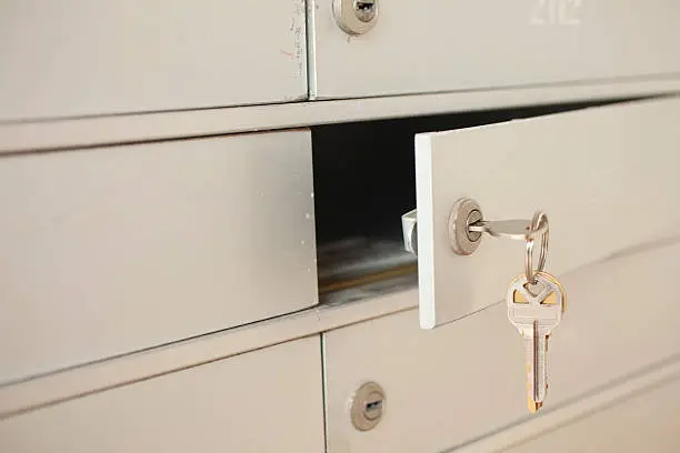 Small gold mailbox key opening, unlocking an apartment mailbox space or safety deposit box at a bank.  Letters inside box.  Close up of mailbox units.   Copyspace.