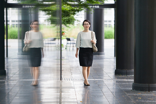 A confident business woman walks to a business meeting. There is a reflection of her in the glass
