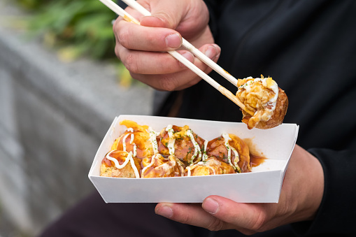 Kyoto iStockalypse.  Closeup of a man eating traditional Japanese cuisine - takoyaki balls from a take out container while people watching on Cat Street (Kyu Shibuya-gawa Promenade) near Harajuku Street, in Tokyo, Japan.  The takoyaki is covered with mayonnaise and teriyaki sauce.