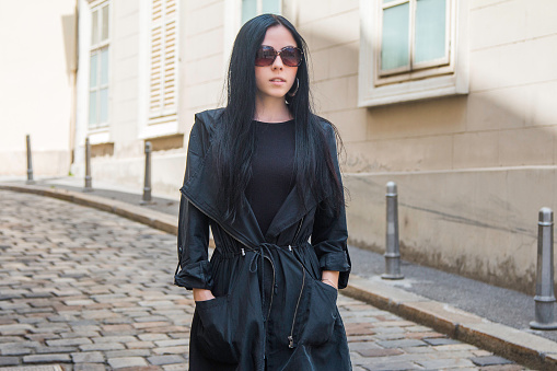 Beautiful black hair girl in black coat and sun glasses walking on street in the old baroque urban ambient