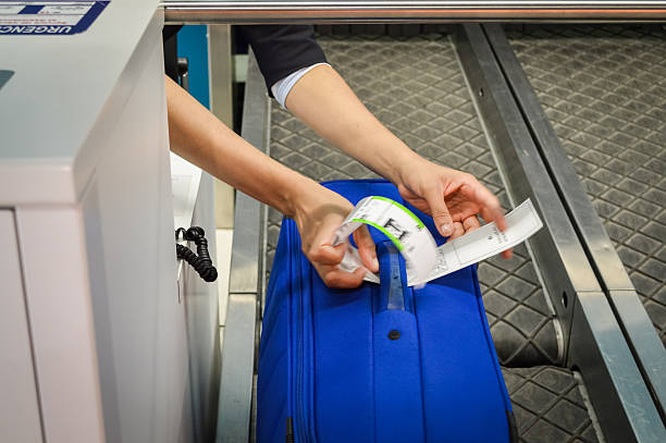 check-in employee attaches a luggage tag check-in employee attaches a luggage tag to suitcase of passenger - close up of hands airport check in counter photos stock pictures, royalty-free photos & images