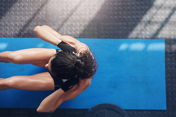 Overhead view of female working out at the gym. Muscular young woman doing sit ups on an exercise mat.