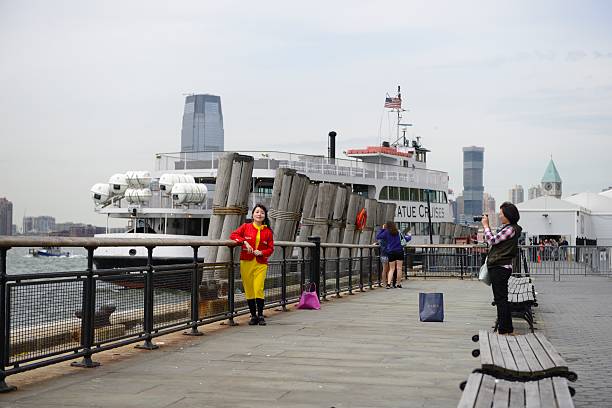 New York, USA - May 10, 2016: Colourful Asian woman posing for a picture. At the background a ferry from Statue Cruises is about to depart from Battery Park to Liberty Island.