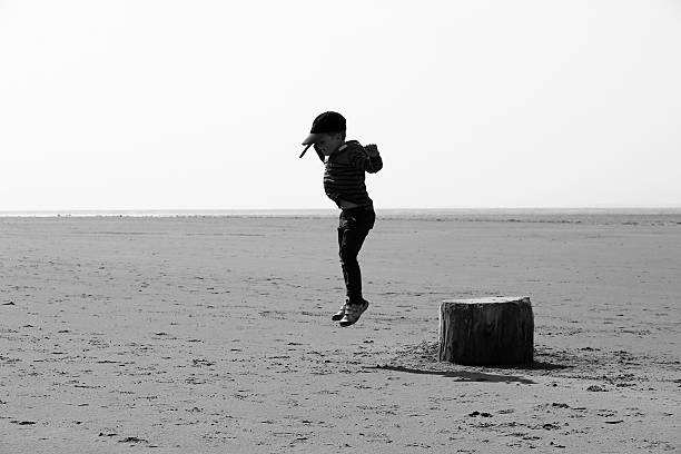 istock Boy jumping off log beach black and white 540739324