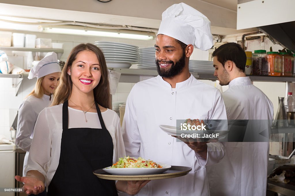 waitress and cooking team at kitchen smiling waitress and cooking team at professional kitchen in restaurant Assistance Stock Photo
