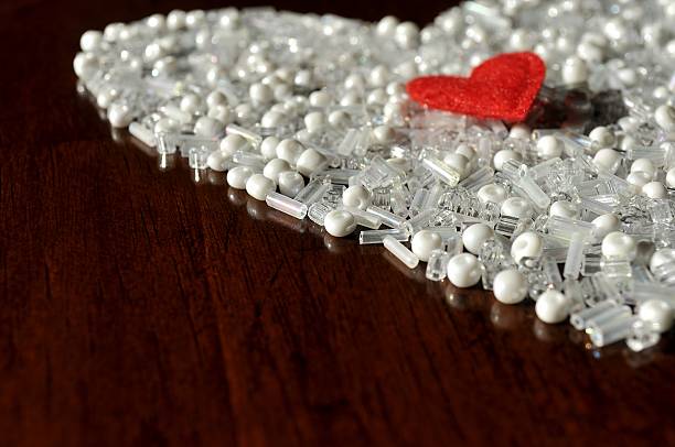 Red heart over the white, pearl beads. Contrast. Side view of heart arranged with variety of white beads. Little red, felt heart on top. Selective focus. Space for text. felt heart shape small red stock pictures, royalty-free photos & images