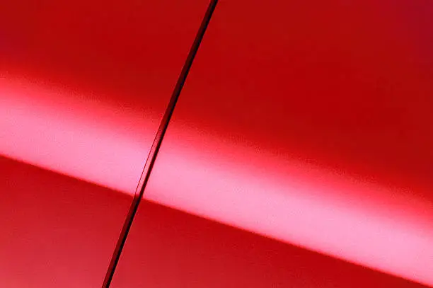 Surface of red sport sedan car, detail of metal fender and door of vehicle bodywork