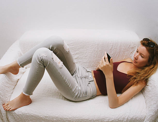 Girl holding cell phone, lies on sofa.
