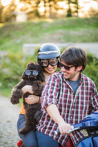 Happy couple on a scooter at summer vacation outdoors at sunset time with their dog. Retro scooter from 1984 year.