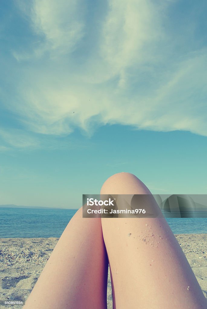 Knees of young woman on the beach; personal pov; retro Toned legs and knees of a young woman lying on the beach, on a sunny summer day. Filtered image in faded, retro, Instagram style; personal POV. Nostalgic concept of summer holidays and travel. Personal Perspective Stock Photo