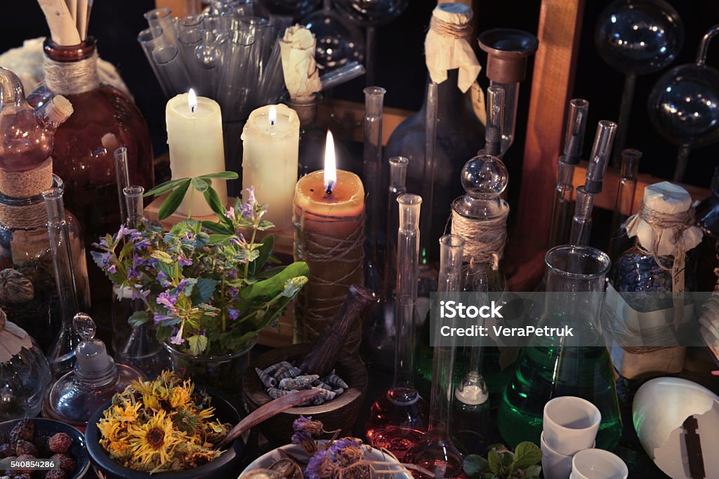 Homeopathic still life with bottles, flasks, old candle and herbs Homeopathic still life with vintage bottles, flasks, burning candle and herbs. Old pharmacy, esoteric or alternative medicine concept. Black magic and occult objects, medieval alchemist ritual Alchemist Stock Photo