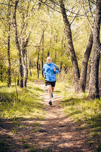A senior man worn in black and blue is running in the forest, during a warm spring day