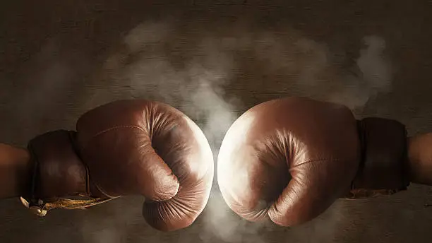 Two brown old boxing gloves hit together