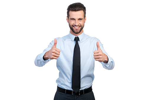 Confident young handsome man in shirt and tie showing his thumbs up and smiling while standing against white background