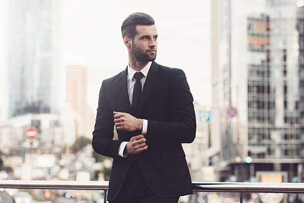 Modern businessman. Confident young man in full suit adjusting his sleeve and looking away while standing outdoors with cityscape in the background well dressed stock pictures, royalty-free photos & images