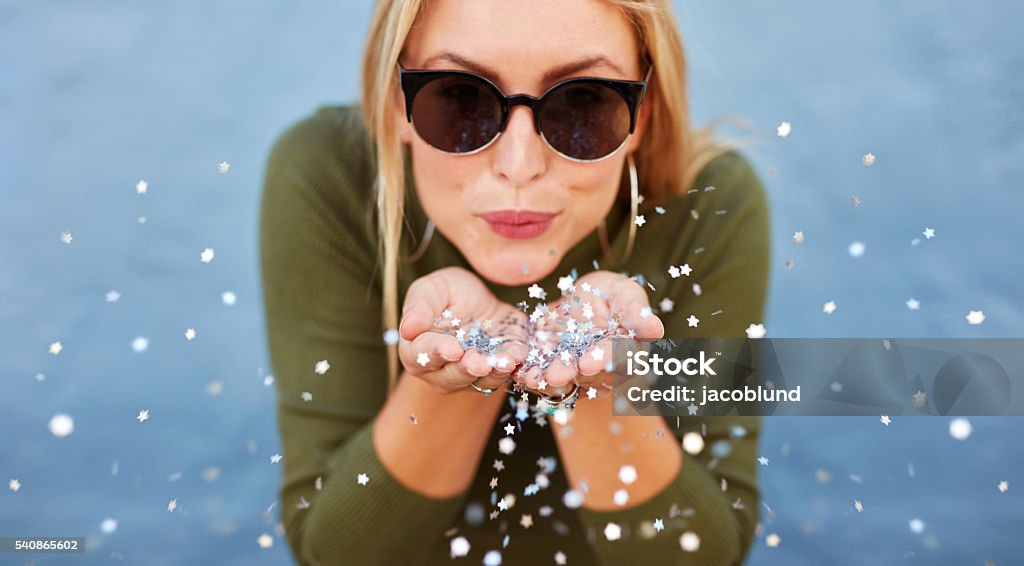 Attractive young woman blowing glitters Close up portrait of attractive young woman blowing glitters. Caucasian Female model having fun over blue background. Women Stock Photo