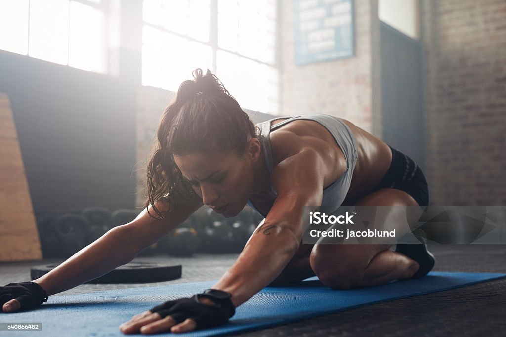Young woman doing yoga on the gym floor Shot of a young woman doing yoga on the gym floor. Muscular female doing stretching workout at health club. Adult Stock Photo
