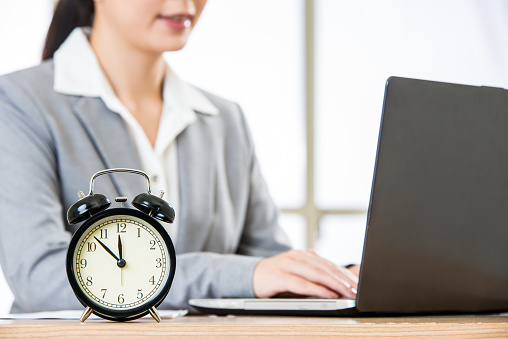 Asian Businesswoman working on laptop with clock showing time