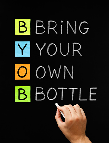 Hand writing BYOB Bring Your Own Bottle with white chalk on blackboard. Acronym often used on party invitations where the alcohol is not provided and you have to bring your own.