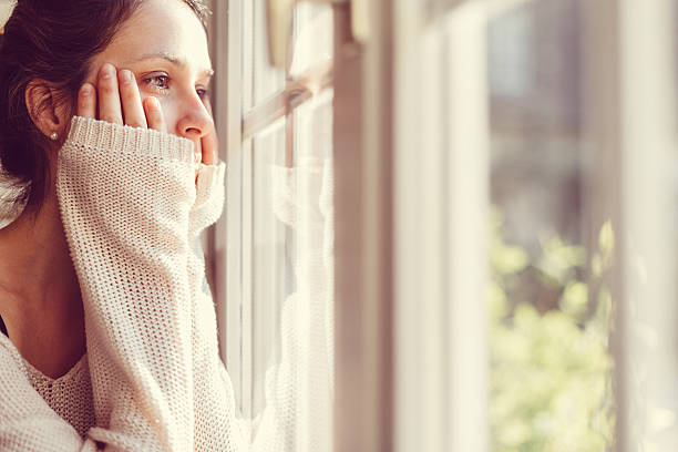 femme regardant à travers la fenêtre - women depression window sadness photos et images de collection