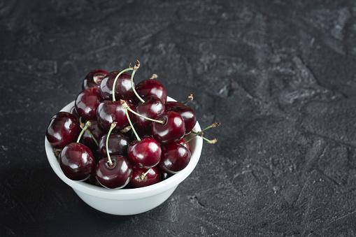 Ripe cherry berries in white plate on concrete background