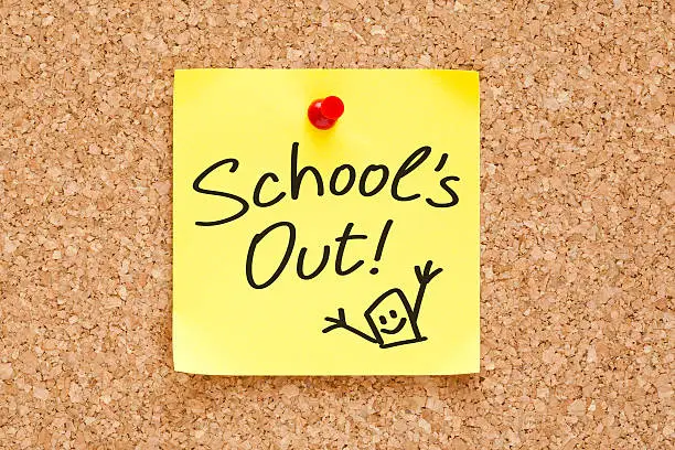 School is Out handwritten on a sticky note pinned on cork bulletin board.