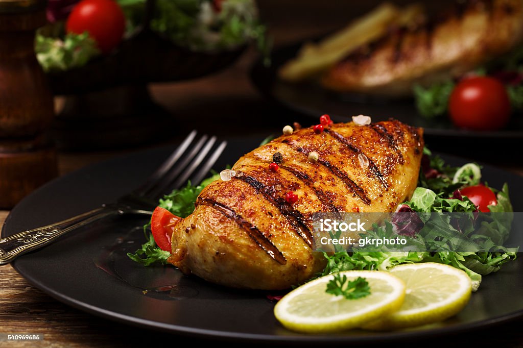grilled chicken breast with green salad and french fries. grilled chicken breast with green salad and french fries on a black plate. Chicken Meat Stock Photo