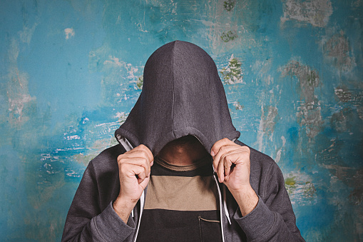 Portrait of shy young man closing covering his face with hands and hoody can't see, hiding. Antisocial and negative human emotion facial expression feeling reaction