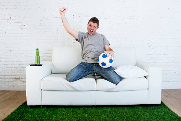istock fan watching television in couch grass pitch carpet celebrating goal 540970834