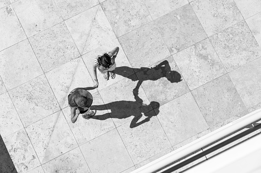 Two teenager girls who talking on the sun in Los Angeles, California. Top view, from directly above, with the focus on the shadows on the tiled ground.